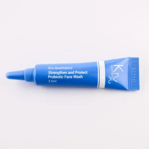 Das Bild zeigt eine auffällige blaue Tube mit einer spitzen Dosierspitze, ebenfalls auf einem beigen Hintergrund. Das Produkt gehört zur KRX Aesthetics-Reihe und trägt den Namen „Strengthen and Protect Probiotic Face Wash“. Der weiße Schriftzug hebt sich gut vom blauen Hintergrund der Tube ab. Die Tube enthält 3,5 ml. Die Beleuchtung ist sanft und gleichmäßig.
