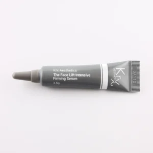 Das Bild zeigt eine ähnliche kleine Tube mit einer spitzen Dosierspitze, ebenfalls auf einem beigen Hintergrund. Das Produkt stammt von KRX Aesthetics und heißt „The Face Lift Intensive Firming Serum“. Die Tube ist schwarz-grau mit weißem Text und einer feinen weißen Linie. Die Füllmenge beträgt 3,5 g. Das Bild hat eine gleichmäßige, sanfte Beleuchtung.