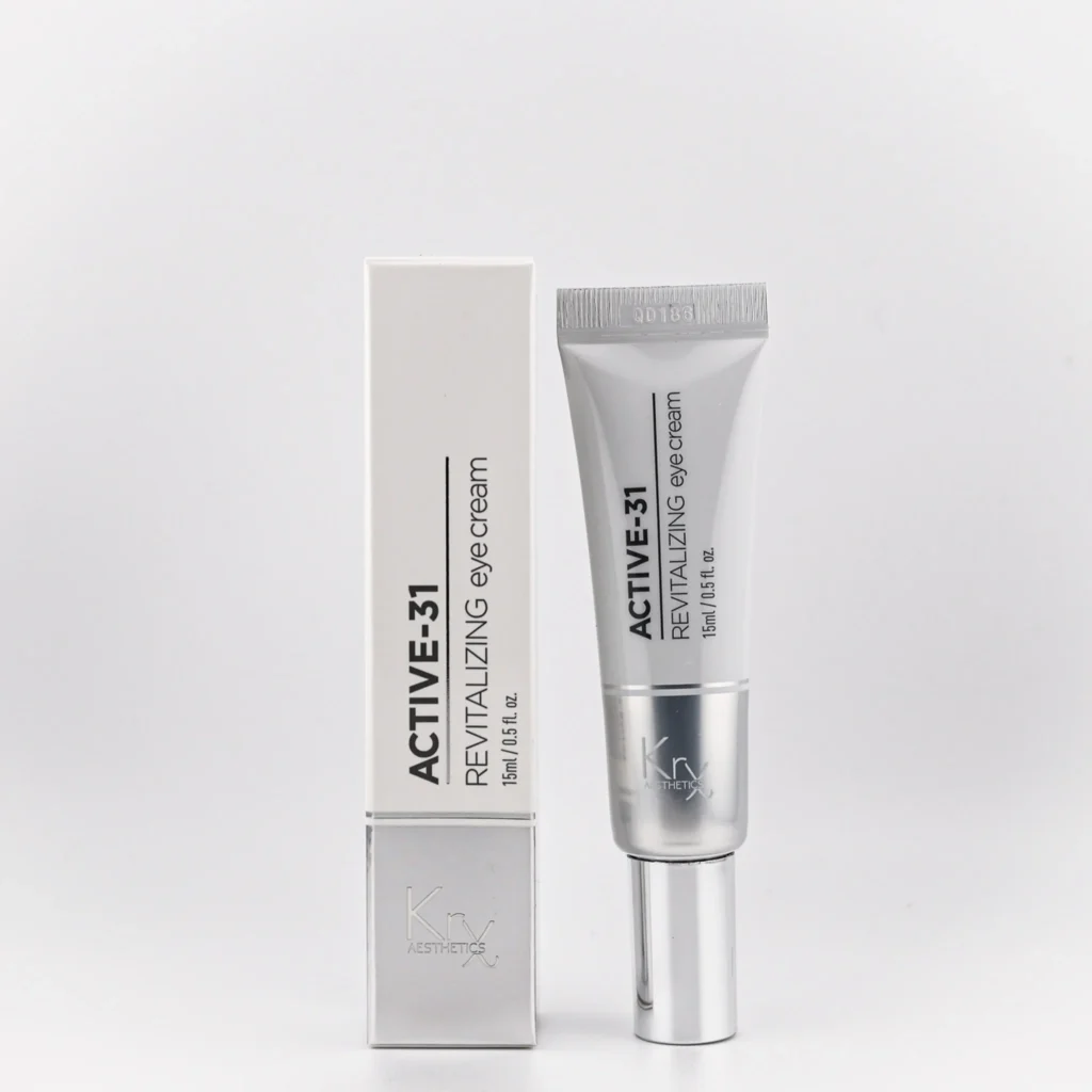 Das Bild zeigt die ACTIVE-31 Revitalizing Eye Cream von Krx Aesthetics. Links befindet sich die Produktverpackung – ein schlanker, silberfarbener Karton mit schwarzer Aufschrift. Rechts daneben ist die passende Tube mit silbernem Applikator zu sehen, ebenfalls in modernem, metallisch wirkendem Design. Auf beiden steht deutlich: ACTIVE-31 Revitalizing eye cream – 15 ml / 0.5 fl. oz. Die Verpackung und Tube wirken hochwertig, elegant und klinisch-professionell.