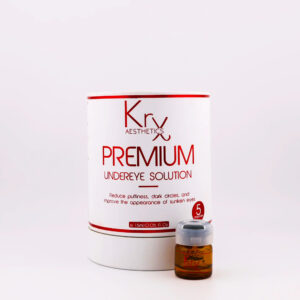 Das Bild zeigt ein Kosmetikprodukt von KrX Aesthetics mit dem Namen PREMIUM Undereye Solution. Die Verpackung ist rund, weiß und trägt ein auffälliges rot-braunes Design. In großen Buchstaben steht auf der Vorderseite: „PREMIUM Undereye Solution“. Darunter ist ein kurzer Hinweis auf die Wirkung des Produkts zu lesen: „Reduce puffiness, dark circles, and improve the appearance of sunken eyes“ – also zur Reduktion von Schwellungen, Augenringen und eingesunkener Augenpartien. Unten auf der Verpackung ist die Mengenangabe „1.5 ml / 0.05 fl. oz.“ aufgeführt. Rechts neben der Verpackung steht eine kleine braune Ampulle mit Schraubdeckel, die offenbar eines der fünf Einzelbehältnisse darstellt, wie durch den Hinweis „5 ampoules“ auf dem Etikett deutlich wird.