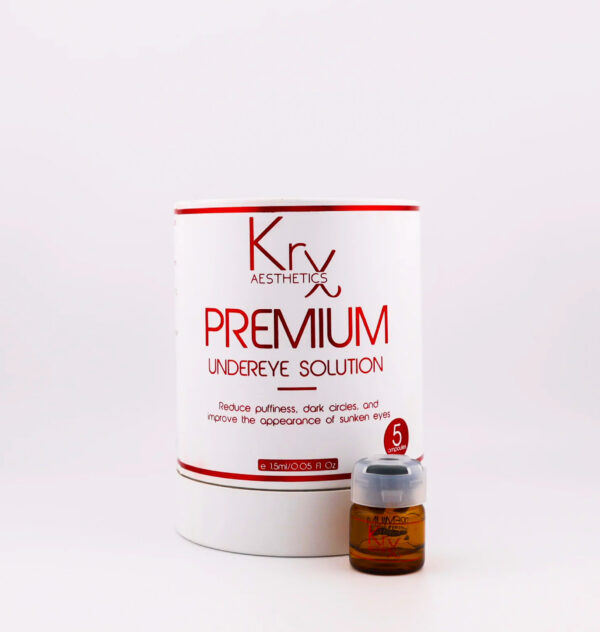 Das Bild zeigt ein Kosmetikprodukt von KrX Aesthetics mit dem Namen PREMIUM Undereye Solution. Die Verpackung ist rund, weiß und trägt ein auffälliges rot-braunes Design. In großen Buchstaben steht auf der Vorderseite: „PREMIUM Undereye Solution“. Darunter ist ein kurzer Hinweis auf die Wirkung des Produkts zu lesen: „Reduce puffiness, dark circles, and improve the appearance of sunken eyes“ – also zur Reduktion von Schwellungen, Augenringen und eingesunkener Augenpartien. Unten auf der Verpackung ist die Mengenangabe „1.5 ml / 0.05 fl. oz.“ aufgeführt. Rechts neben der Verpackung steht eine kleine braune Ampulle mit Schraubdeckel, die offenbar eines der fünf Einzelbehältnisse darstellt, wie durch den Hinweis „5 ampoules“ auf dem Etikett deutlich wird.
