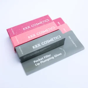 Das Bild zeigt mehrere farbenfrohe rechteckige Verpackungen der Marke KRX COSMETICS, die übereinandergelegt sind. Die Kartons sind in verschiedenen Farbtönen gehalten – darunter Pink, Hellrosa und Dunkelgrau. Auf jeder Verpackung steht in großer weißer Schrift der Markenname KRX COSMETICS. Auf der dunkelgrauen Verpackung ist zusätzlich der Produktname Pocket Filler – Lip Plumping Gloss sowie der Hinweis With SenseHot™ zu lesen. Das Design ist modern und jugendlich mit einem dezenten Molekülmuster im Hintergrund, was auf kosmetisch-wissenschaftlich entwickelte Inhaltsstoffe hinweist.