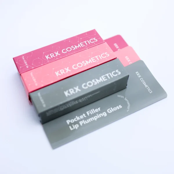 Das Bild zeigt mehrere farbenfrohe rechteckige Verpackungen der Marke KRX COSMETICS, die übereinandergelegt sind. Die Kartons sind in verschiedenen Farbtönen gehalten – darunter Pink, Hellrosa und Dunkelgrau. Auf jeder Verpackung steht in großer weißer Schrift der Markenname KRX COSMETICS. Auf der dunkelgrauen Verpackung ist zusätzlich der Produktname Pocket Filler – Lip Plumping Gloss sowie der Hinweis With SenseHot™ zu lesen. Das Design ist modern und jugendlich mit einem dezenten Molekülmuster im Hintergrund, was auf kosmetisch-wissenschaftlich entwickelte Inhaltsstoffe hinweist.