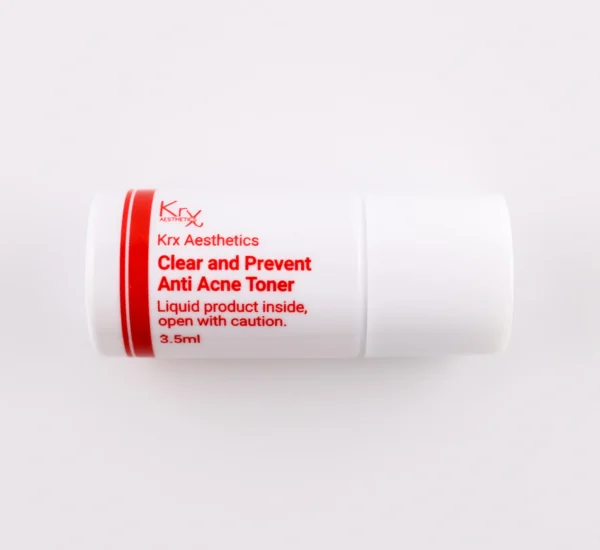 Das Bild zeigt einen kleinen, weißen Zylinderbehälter mit einem Drehverschluss, liegend auf einem beigen Hintergrund. Das Produkt gehört zur KRX Aesthetics-Reihe und trägt den Namen „Clear and Prevent Anti Acne Toner“. Der Behälter hat eine rote Beschriftung und enthält 3,5 ml Flüssigkeit. Zusätzlich steht auf dem Etikett: „Liquid product inside, open with caution.“ Die Beleuchtung ist weich und gleichmäßig.