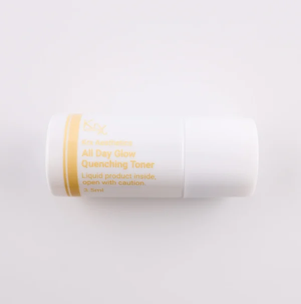 Dieses Bild zeigt einen weiteren kleinen, weißen Zylinderbehälter mit einer goldenen Beschriftung. Das Produkt gehört zur KRX Aesthetics-Reihe und heißt „All Day Glow Quenching Toner“. Es enthält 3,5 ml Flüssigkeit und trägt dieselbe Warnung wie die anderen Toner: „Liquid product inside, open with caution.“ Der Hintergrund ist beige, und die Beleuchtung ist gleichmäßig.