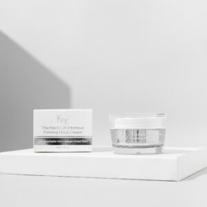 Ein rundes, durchsichtiges Glas mit einem silbernen Deckel, daneben eine weiße Verpackung mit schwarzer Schrift. Das Produkt „The Neck Lift Intensive Firming Cream“ von KRX Aesthetics ist darauf abgebildet. Die Creme enthält absorbierbare Mikro-Kollagen-Fasern und kommt in einer 50-ml-Packung.