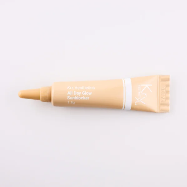 Hier ist eine weitere beige Tube mit einer spitzen Dosierspitze zu sehen. Das Produkt gehört zur KRX Aesthetics-Reihe und trägt den Namen „All Day Glow Sunblocker“. Die Tube hat eine weiße Beschriftung und enthält 3,5 g des Produkts. Das Produkt liegt auf einem beigen Hintergrund mit gleichmäßiger Beleuchtung.