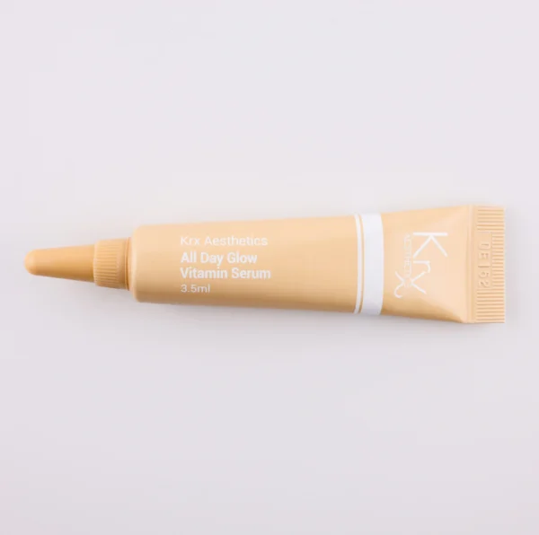 Dieses Bild zeigt eine beige Tube mit einer spitzen Dosierspitze auf einem beigen Hintergrund. Das Produkt stammt von KRX Aesthetics und heißt „All Day Glow Vitamin Serum“. Die Tube hat eine weiße Beschriftung mit einer dünnen weißen Linie und enthält 3,5 g. Die Beleuchtung ist sanft und gleichmäßig.