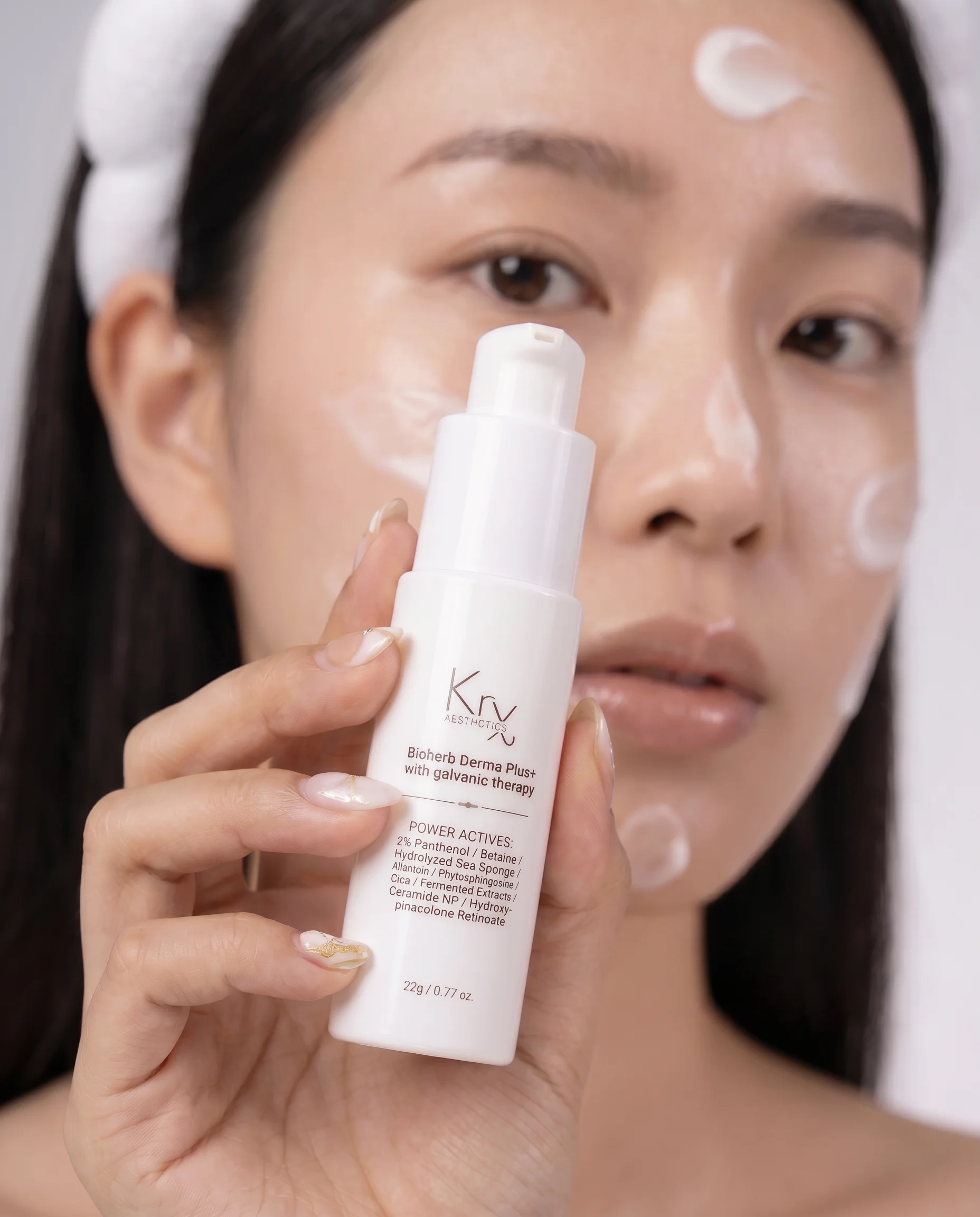 Frau mit Serum auf Stirn, Wangen und Kinn hält einen Pumpspender von KRX Aesthetics BIOHERB DERMA PLUS+.