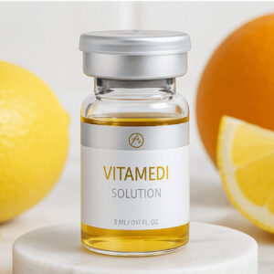 Das Bild zeigt ein kleines, transparentes Glasfläschchen mit goldgelber Flüssigkeit. Auf dem Fläschchen steht in klarer, moderner Schrift: VITAMEDI SOLUTION. Darunter ist die Füllmenge angegeben: 5 ml / 0.17 fl. oz.. Die Ampulle ist mit einem silberfarbenen Deckel verschlossen und steht auf einer hellen, runden Steinplatte. Im Hintergrund sind unscharf eine Zitrone, eine Orangenscheibe und weitere gelb-orangene Zitrusfrüchte zu erkennen, was auf einen frischen, vitaminreichen Inhalt hindeutet. Das Gesamtbild wirkt clean, ästhetisch und hochwertig inszeniert.