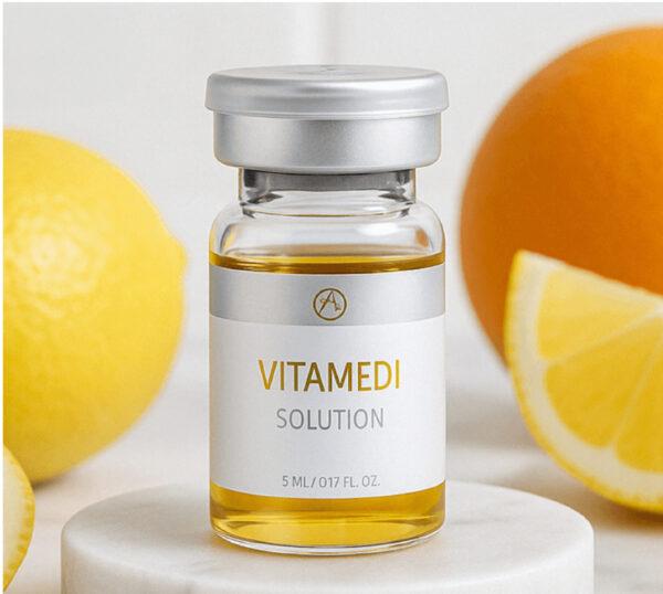 Das Bild zeigt ein kleines, transparentes Glasfläschchen mit goldgelber Flüssigkeit. Auf dem Fläschchen steht in klarer, moderner Schrift: VITAMEDI SOLUTION. Darunter ist die Füllmenge angegeben: 5 ml / 0.17 fl. oz.. Die Ampulle ist mit einem silberfarbenen Deckel verschlossen und steht auf einer hellen, runden Steinplatte. Im Hintergrund sind unscharf eine Zitrone, eine Orangenscheibe und weitere gelb-orangene Zitrusfrüchte zu erkennen, was auf einen frischen, vitaminreichen Inhalt hindeutet. Das Gesamtbild wirkt clean, ästhetisch und hochwertig inszeniert.