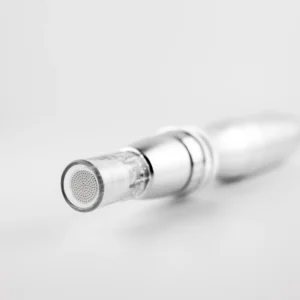 Das Bild zeigt die Nahaufnahme einer kosmetischen oder medizinischen Gerätespitze – vermutlich ein Aufsatz für ein Microneedling- oder Meso-Gerät. Die Spitze ist rund und durchsichtig, mit einer Vielzahl fein angeordneter Mikroöffnungen oder Mikronadeln. Der Aufsatz ist aus Kunststoff und Metall gefertigt, wirkt technisch präzise und hochwertig verarbeitet. Im Hintergrund ist der Rest des Geräts nur verschwommen sichtbar.