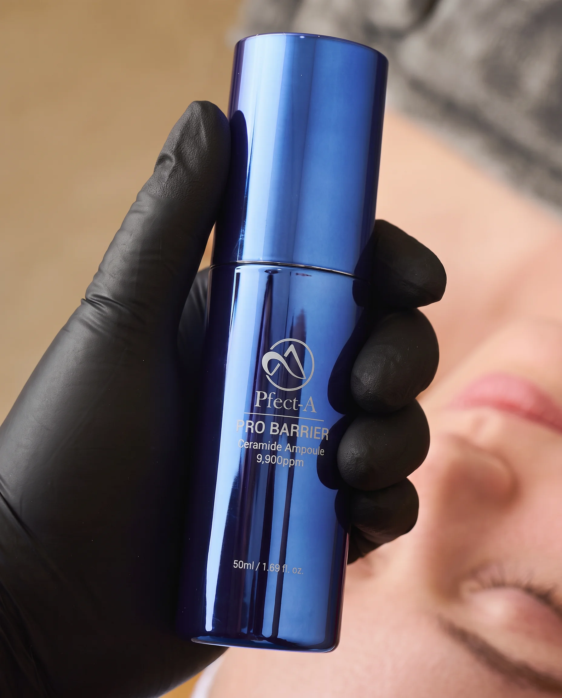 Pfect-A Pro Barrier Ceramide Ampoule wird mit einem Handschuh vor dem Gesicht einer Kundin gehalten